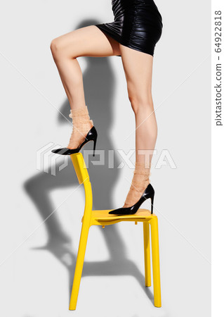 Cropped image of slim female legs in tulle socks and black stilettos on yellow chair Cropped image of slim female legs in tulle socks and black stilettos on yellow chair 64922818