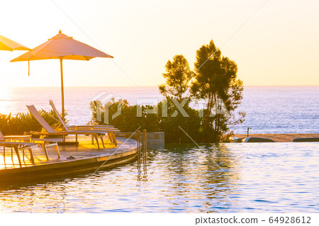 Beautiful tropical outdoor beach sea ocean with umbrella and chiar around outdoor swimming pool at sunset or sunrise time 64928612