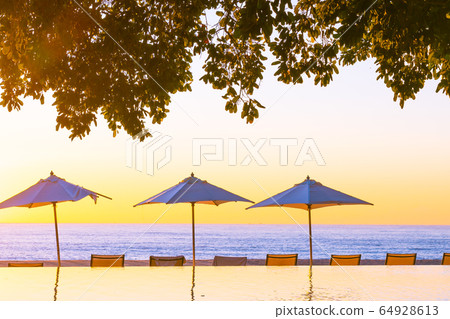 Beautiful tropical outdoor beach sea ocean with umbrella and chiar around outdoor swimming pool at sunset or sunrise time 64928613