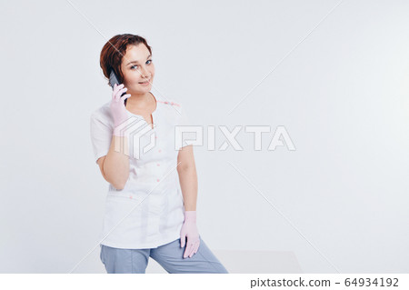a doctor in gloves is talking on the phone on a white background. A woman learns the techniques of business planning on quarantine, protection from coronavirus, virus a doctor in gloves is talking on the phone on a white background. A woman learns the techniques of business planning on quarantine, protection from coronavirus, virus 64934192