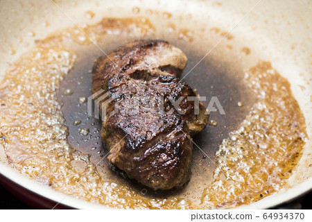 Grilling beef fillet steak in a frying pan 64934370