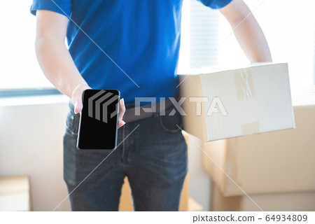 Young delivery man in uniform holding and showing Young delivery man in uniform holding and showing 64934809