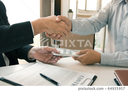 Two corporate businessmen shaking hands while one Two corporate businessmen shaking hands while one 64935957