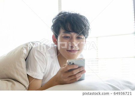 看在被褥的一個微笑的年輕人智能手機 64936721