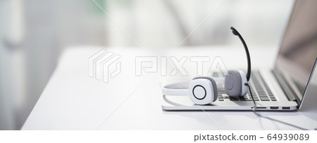 Laptop, headphones with microphone on table defocused background. 64939089