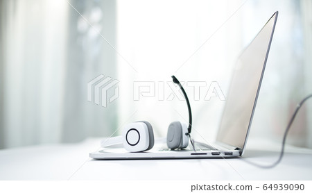 Close-up of laptop, white headphones with microphone on bokeh background. Close-up of laptop, white headphones with microphone on bokeh background. 64939090