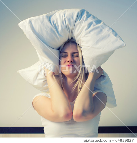 Young woman covering ears with pillow because of 64939827