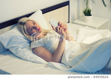 young woman on bed late at night texting using 64939828
