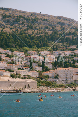 A group of tourists travel in pairs kayaks by sea against the backdrop of a cruise ship and the coast, near old town of Dubrovnik, Croatia. Concept banner travel. Aerial top view. A group of tourists travel in pairs kayaks by sea against the backdrop of a cruise ship and the coast, near old town of Dubrovnik, Croatia. Concept banner travel. Aerial top view. 64939952