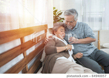 Asian Senior Woman taking medicines and drinking water while sitting on couch. Asian Senior Woman taking medicines and drinking water while sitting on couch. 64940057