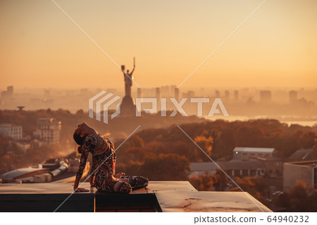 Woman doing yoga on the roof of a skyscraper in big city. 64940232