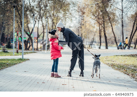 Happy mother and her daughter walk with dog in autumn park Happy mother and her daughter walk with dog in autumn park 64940975
