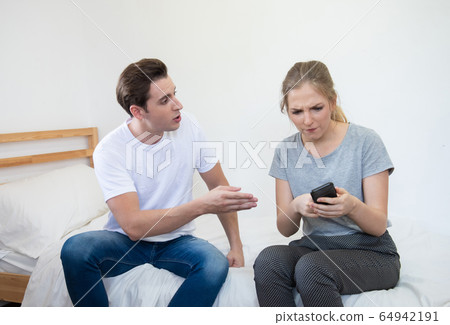 caucasian couple argue with phone on bed at home 64942191