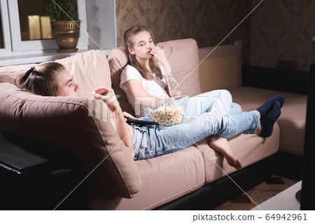 Attractive young long-haired couple hugging on a sofa at home in isolation watching tv. The concept of spending time with loved ones during a pandemic Attractive young long-haired couple hugging on a sofa at home in isolation watching tv. The concept of spending time with loved ones during a pandemic 64942961