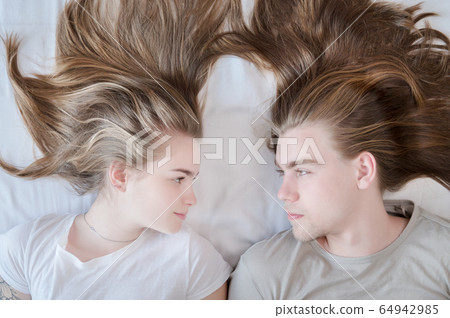 Top view portrait of a young couple with long hair lying on the bed and looking at each other. Top view portrait of a young couple with long hair lying on the bed and looking at each other. 64942985