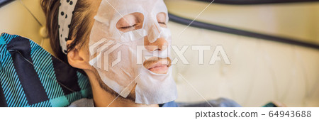 Young man doing facial mask sheet. Beauty and Skin Care Concept BANNER, LONG FORMAT Young man doing facial mask sheet. Beauty and Skin Care Concept BANNER, LONG FORMAT 64943688