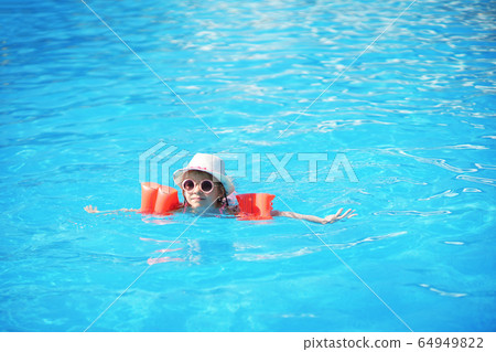 A charming child of European appearance, a girl 7-8 years old, swimming in the pool. Summer, a clear and sunny day. A girl with her family on vacation at sea. The girl has inflatable arm ruffles A charming child of European appearance, a girl 7-8 years old, swimming in the pool. Summer, a clear and sunny day. A girl with her family on vacation at sea. The girl has inflatable arm ruffles 64949822