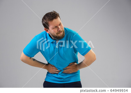 Young man suffers from pain, feels sick, ill and weakness isolted on studio background Young man suffers from pain, feels sick, ill and weakness isolted on studio background 64949934