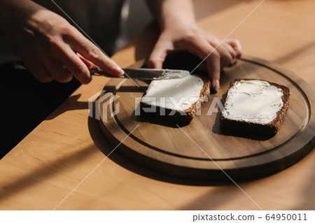 Close up of female butter the rye toasted bread by vegan butter. Woman butter toast at home on wooden board 64950011