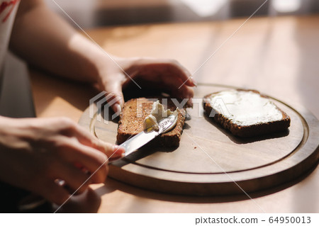 Close up of female butter the rye toasted bread by vegan butter. Woman butter toast at home on wooden board 64950013