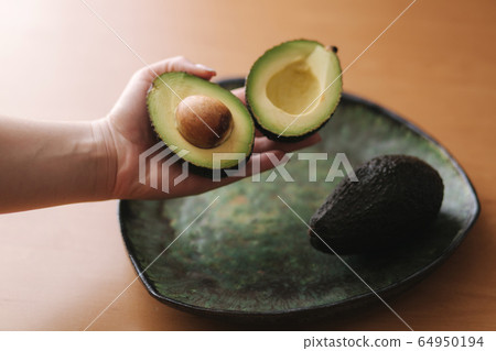 Fresh sliced avocado in woman's hand on green plate. Vegetarian food concept Fresh sliced avocado in woman's hand on green plate. Vegetarian food concept 64950194