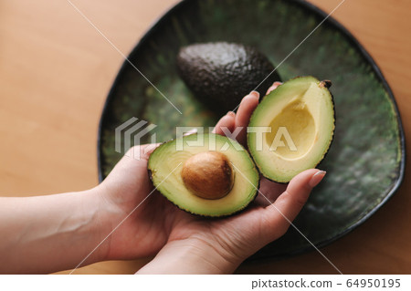 Fresh sliced avocado in woman's hand on green plate. Vegetarian food concept 64950195