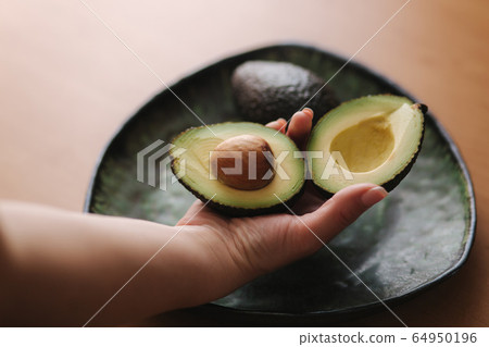 Fresh sliced avocado in woman's hand on green plate. Vegetarian food concept 64950196