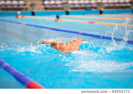 Athletic man swimming in butterfly style in the swimming pool with clear blue water. 64950773
