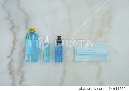 Blue Ethyl Alcohol spray bottle, Alcohol gel bottle, Alcohol in plastic bottle and blue surgical masks on the marble desk. Coronavirus Protection Set. Blue Ethyl Alcohol spray bottle, Alcohol gel bottle, Alcohol in plastic bottle and blue surgical masks on the marble desk. Coronavirus Protection Set. 64951211