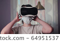 A young woman in a mask on self-isolation during a coronavirus pandemic uses virtual reality glasses for work and entertainment. 64951537