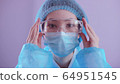 Asian woman doctor in a mask and a protective suit puts on safety glasses and looks at the camera. Coronavirus epidemic, concept. 64951545