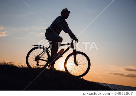 silhouette of a hipster man on a bicycle on sunset silhouette of a hipster man on a bicycle on sunset 64951867