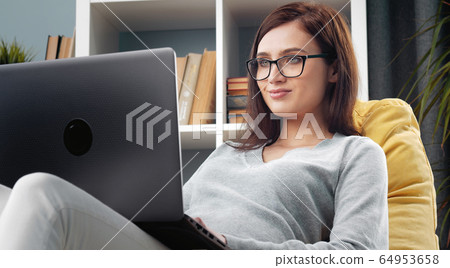 Brunette sitting beanbag with laptop 64953658