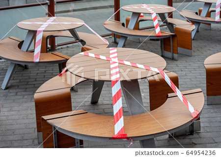 Outdoor cafe/restaurant is closed for quarantine during coronavirus epidemic. Access to restaurant, cafe is prohibited for duration of pandemic, seats are blocked with a warning tape 64954236