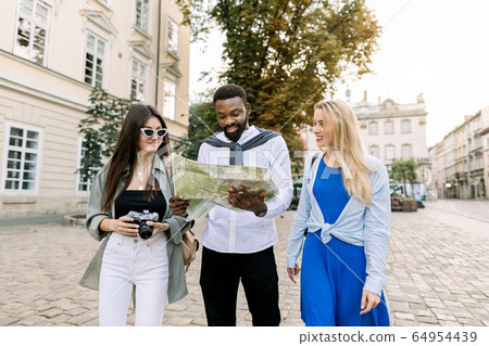 Group of young happy multiracial tourists, African man and two Caucasian girls, looking for some destination with city map and enjoying their vacation. People,fun,happiness and travel concept Group of young happy multiracial tourists, African man and two Caucasian girls, looking for some destination with city map and enjoying their vacation. People,fun,happiness and travel concept 64954439