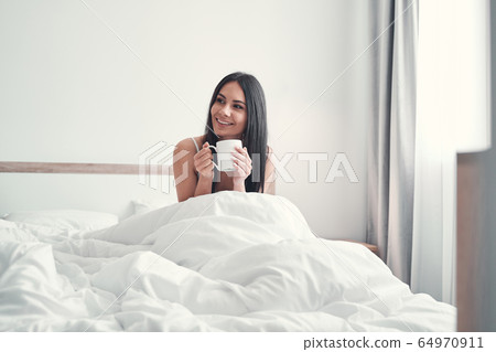 Positive delighted longhaired girl drinking hot tea Positive delighted longhaired girl drinking hot tea 64970911