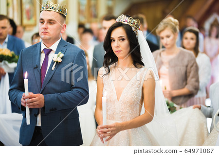 Bride and groom holding candles in church 64971087