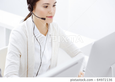 Call center. Casual dressed woman sitting and working in headset at customer service office. Business concept Call center. Casual dressed woman sitting and working in headset at customer service office. Business concept 64972136