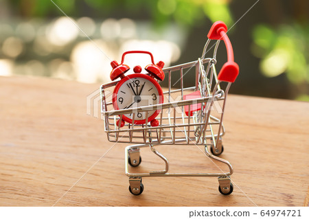 Fast delivery, time value of money concept : Red analog clock in a red - silver shopping cart or a supermarket shopping basket on wooden table. depicts the importance of time in our daily life. 64974721