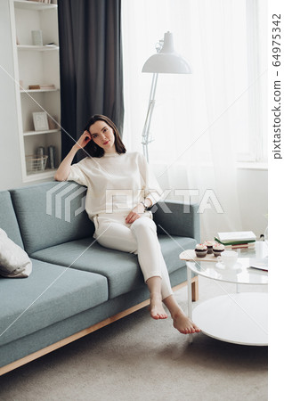 Handsome young woman sits on a big sofa and thinks 64975342