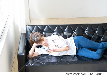A woman relaxing while touching a smartphone A woman relaxing while touching a smartphone 64978093