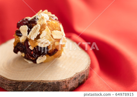 One healthy homemade energy ball made from pieces of dried cranberries and apricots and oat flakes on wooden saw cut on red fabric. Close-up wholesome sweets, selective focus. 64978915