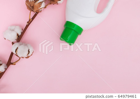 Liquid washing detergent in plastic bottle and cotton flowers on pink background. Liquid washing detergent in plastic bottle and cotton flowers on pink background. 64979461
