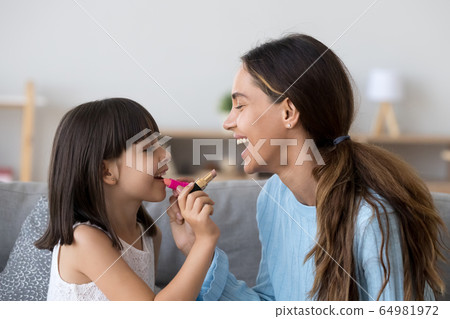 Smiling mom and happy kid daughter doing makeup together Smiling mom and happy kid daughter doing makeup together 64981972