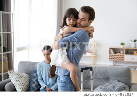 Sad little girl upset by father leaving embracing dad 64982024