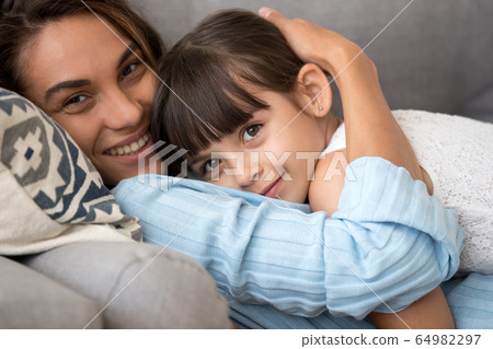 Loving mom embracing adorable kid daughter relaxing on sofa, por 64982297