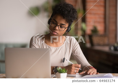 Focused mixed race woman wearing headphones watching webinar write notes Focused mixed race woman wearing headphones watching webinar write notes 64983174