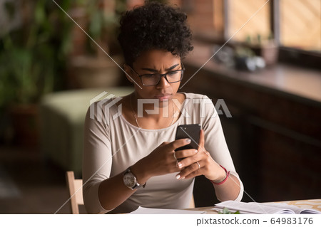 Upset confused african woman holding cellphone having problem with phone Upset confused african woman holding cellphone having problem with phone 64983176