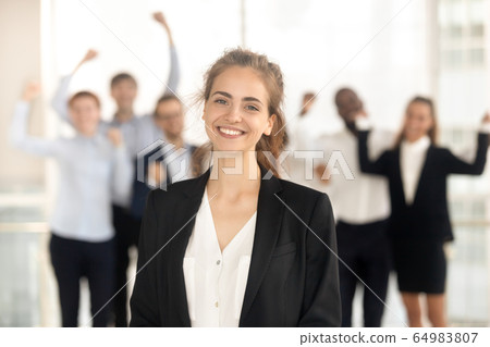 Proud lady leader looking at camera while team celebrating victory Proud lady leader looking at camera while team celebrating victory 64983807