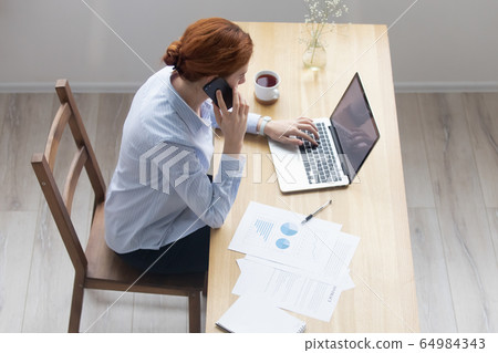 Businesswoman using laptop talking on phone in office, top view Businesswoman using laptop talking on phone in office, top view 64984343